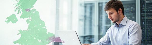 IT engineer reviewing a UK support coverage map beside a laptop in a Central Bedfordshire office